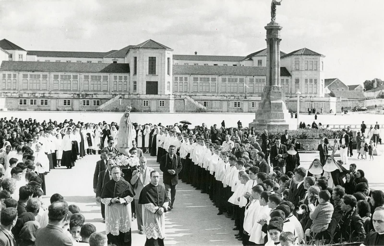1955 年法蒂瑪聖殿廣場上的聖母像遊行，神職人員與信眾夾道，背景是玫瑰聖母聖殿的長廊與高柱