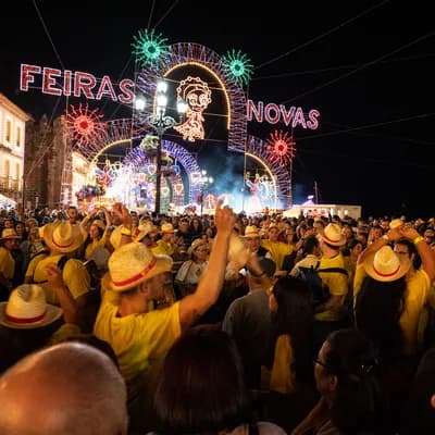 夜裡的燈飾拱門寫著 FEIRAS NOVAS，底下擠滿戴草帽的人群