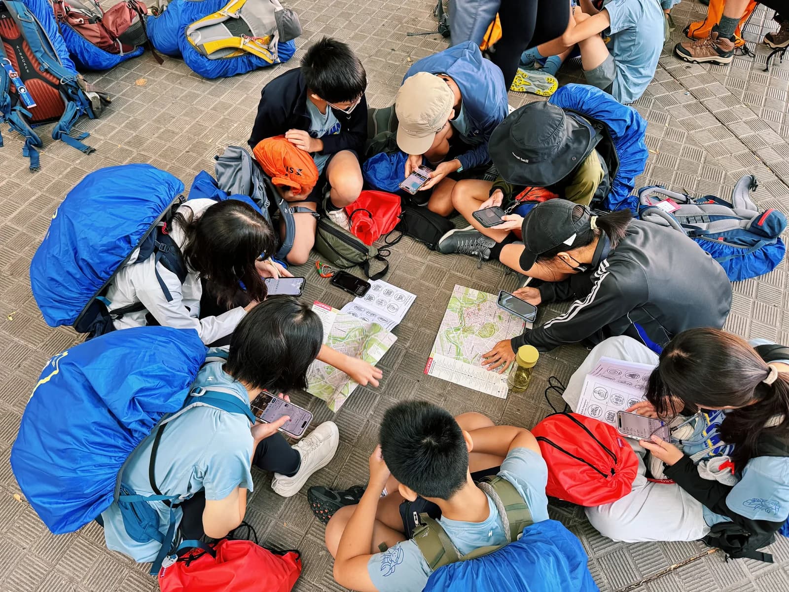 學生圍坐在背包旁，共同查看地圖、紙本資料與手機