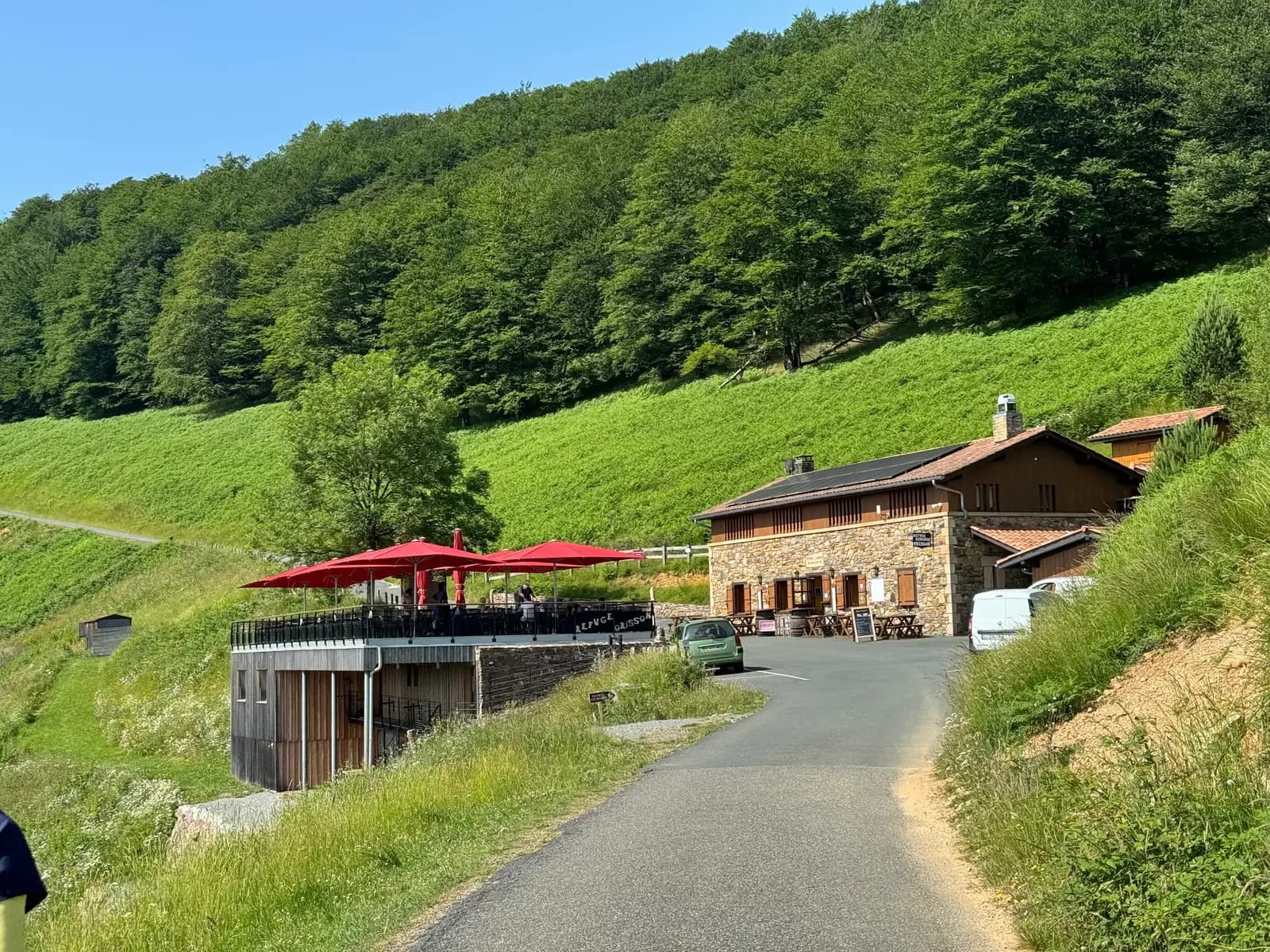 庇里牛斯山坡上的 Refuge Orisson 庇護所，紅色陽傘的露臺與通往山上的柏油小路